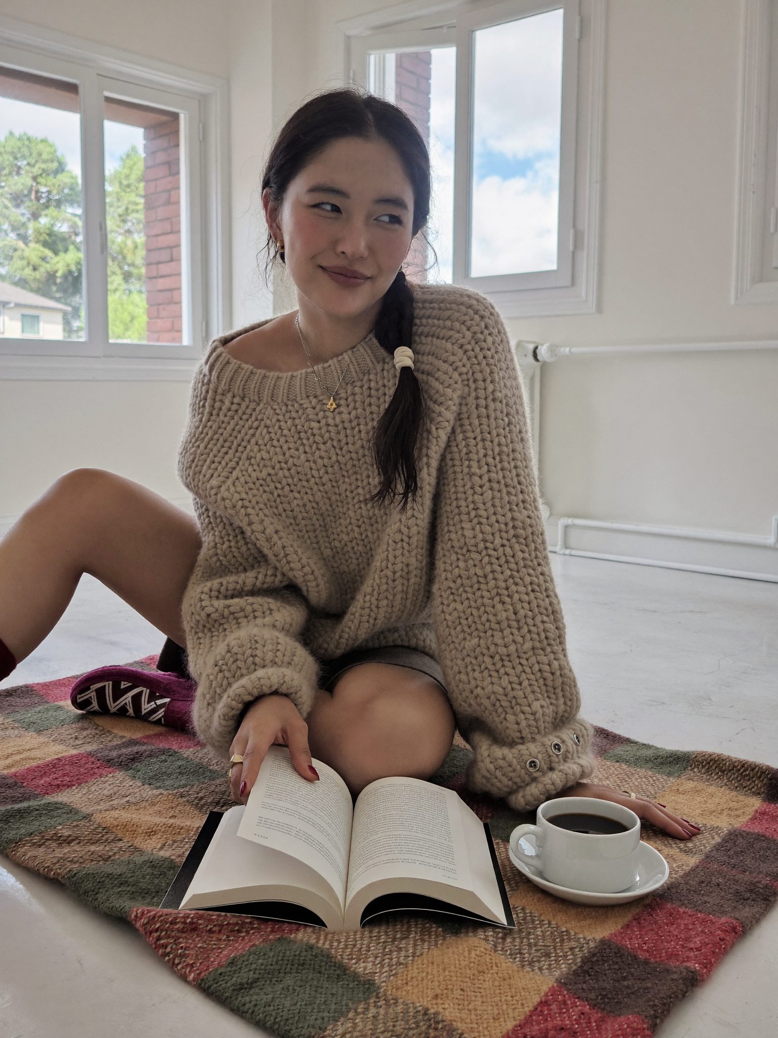 Девушка в свитере с чашкой кофе и книгой на пледе