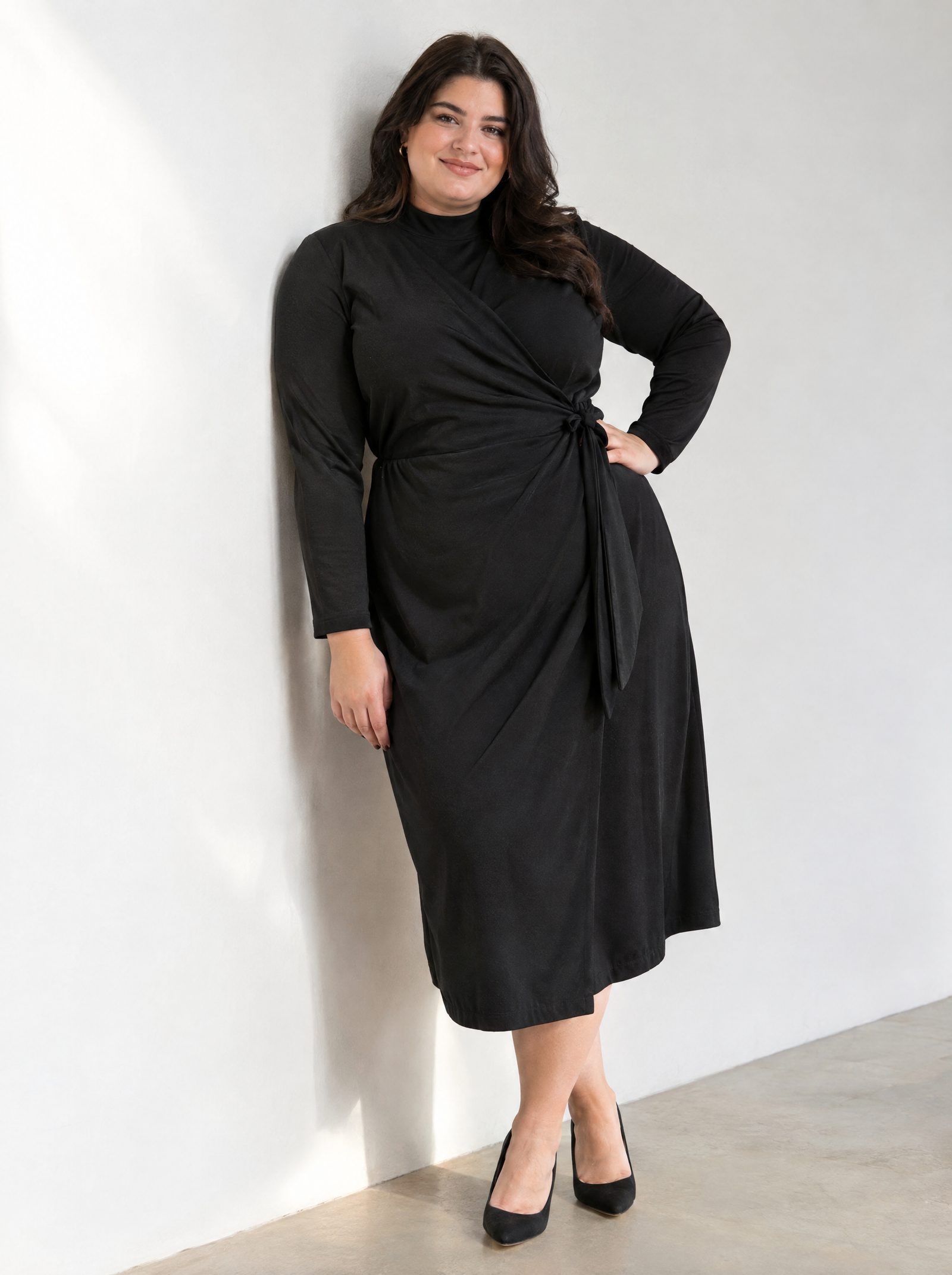 Девушка plus size стоит, опираясь плечом о стену, рука на талии