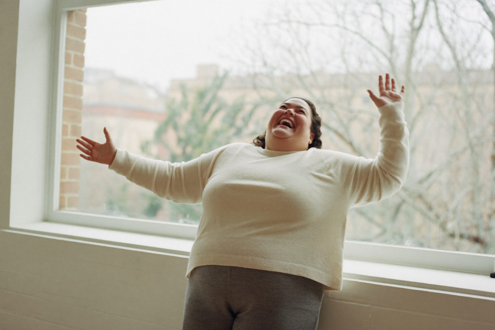 Девушка plus size смеётся у большого окна в мягком свете